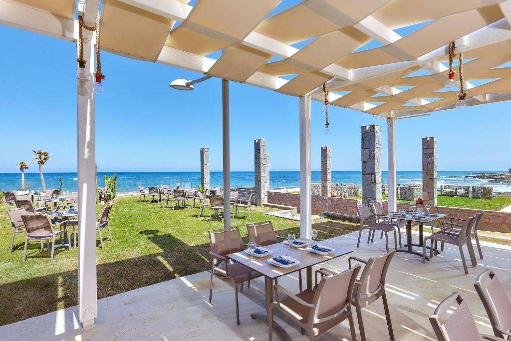 a patio with tables and chairs and the ocean in the background at St Constantin Sea Hotel & Spa Resort in Gouves