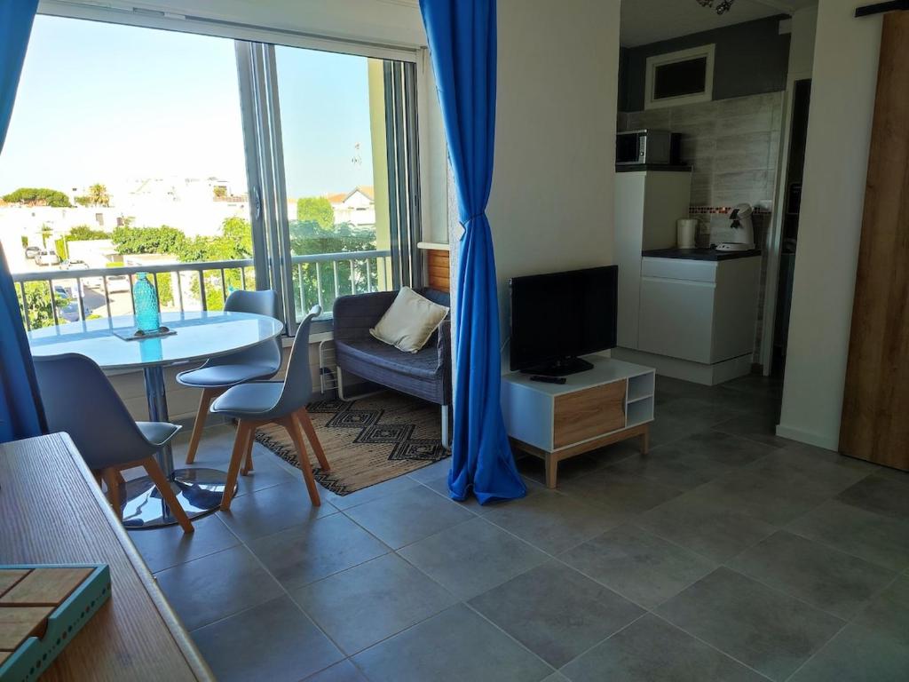 un salon avec une télévision et une table avec des chaises dans l'établissement Studio avec coin nuit à deux pas de la plage, à Mauguio