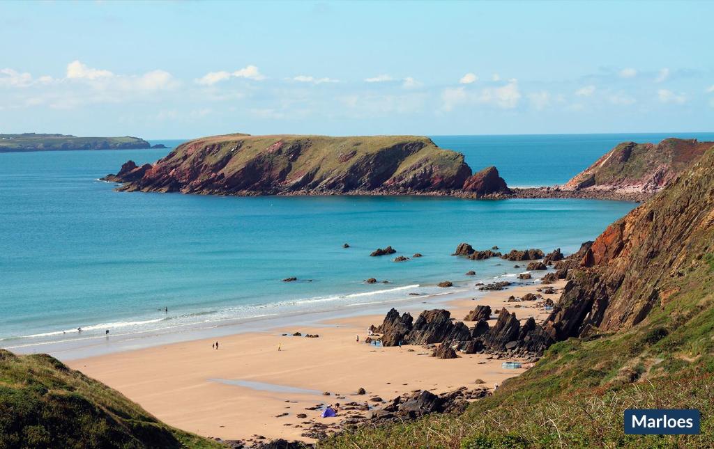 une plage avec des gens dans l'eau et des falaises dans l'établissement Kittiwake Cottage, à Marloes