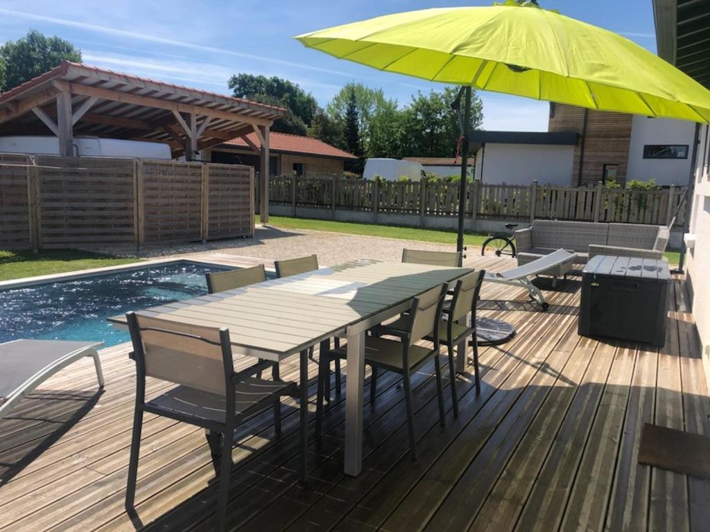 une terrasse en bois avec une table et un parasol jaune dans l'établissement Maison famille avec piscine, Wi-Fi et parking à Gujan-Mestras - FR-1-319-583, à Gujan-Mestras