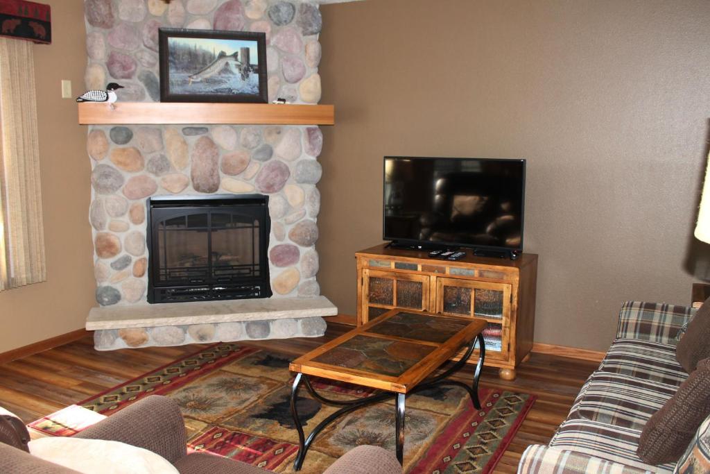 a living room with a stone fireplace and a tv at 2 Bedroom Lower Lakefront Condo, Wild Eagle Lodge #116 in Eagle River