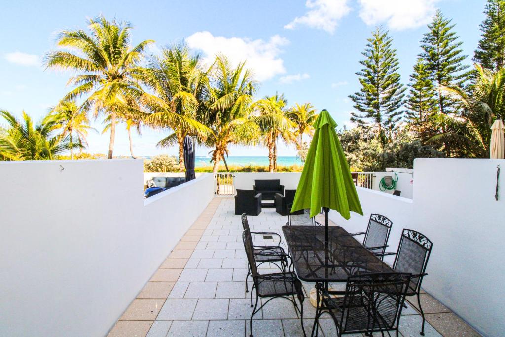 a patio with chairs and a green umbrella and palm trees at Castle Th16 Beachfront Townhouse with private patio, direct beach access, pool, tennis & free parking! in Miami Beach