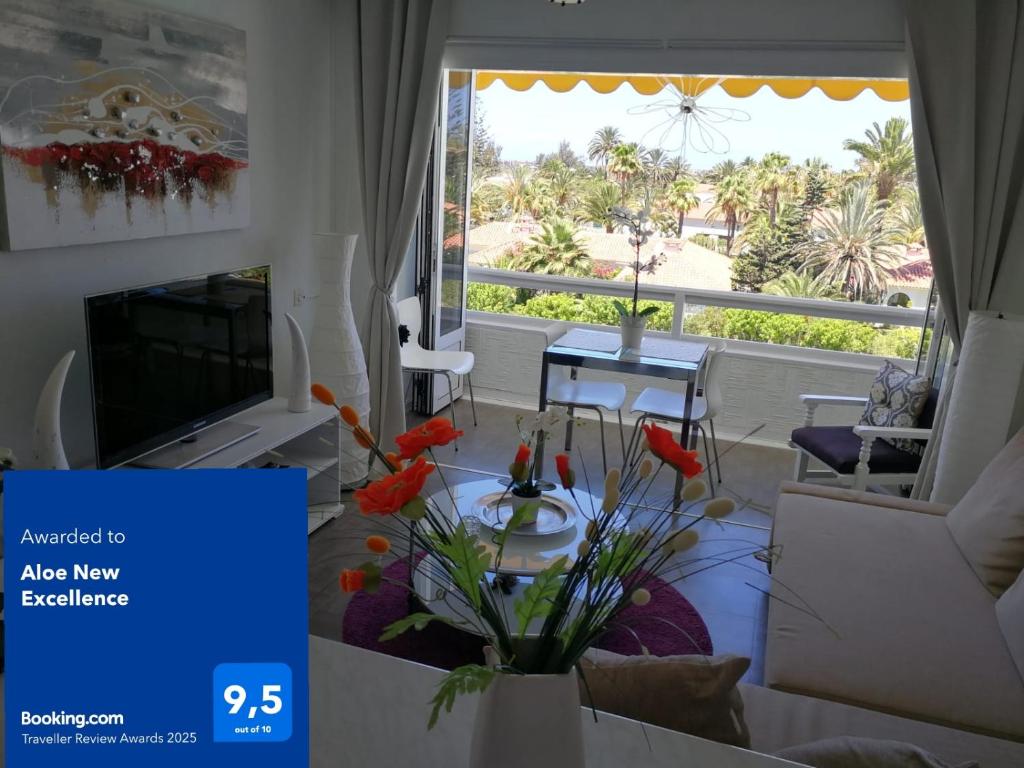 - un salon avec une télévision et une table fleurie dans l'établissement Aloe New Excellence, à Playa del Ingles