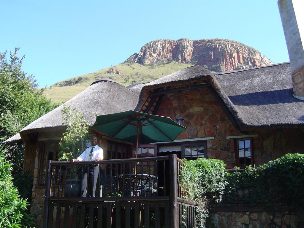 un hombre parado en un balcón frente a una casa en Forest Creek Lodge & Spa, en Badfontein