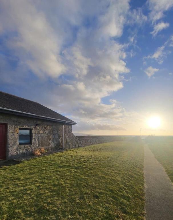a stone building in a field with the sun in the sky at The Wee House -Coorie Doon Stays in Troon