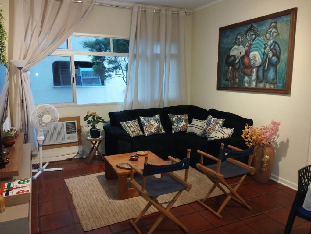 a living room with a black couch and chairs at Apê Retrô com Wi-Fi e Vaga - 350 m da Praia da Enseada in Guarujá