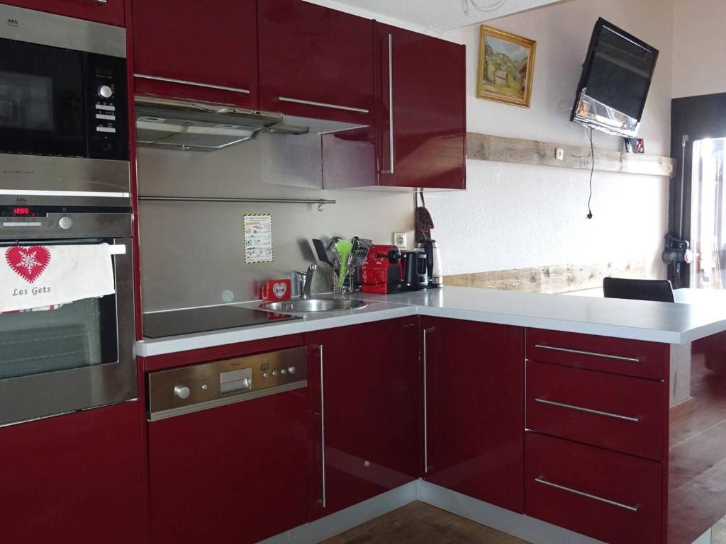 une cuisine avec armoires rouges et appareils en acier inoxydable dans l'établissement Duplex 4 pièces, 8 pers, confortable, rue du centre, garage, plein sud - FR-1-802-95, aux Gets