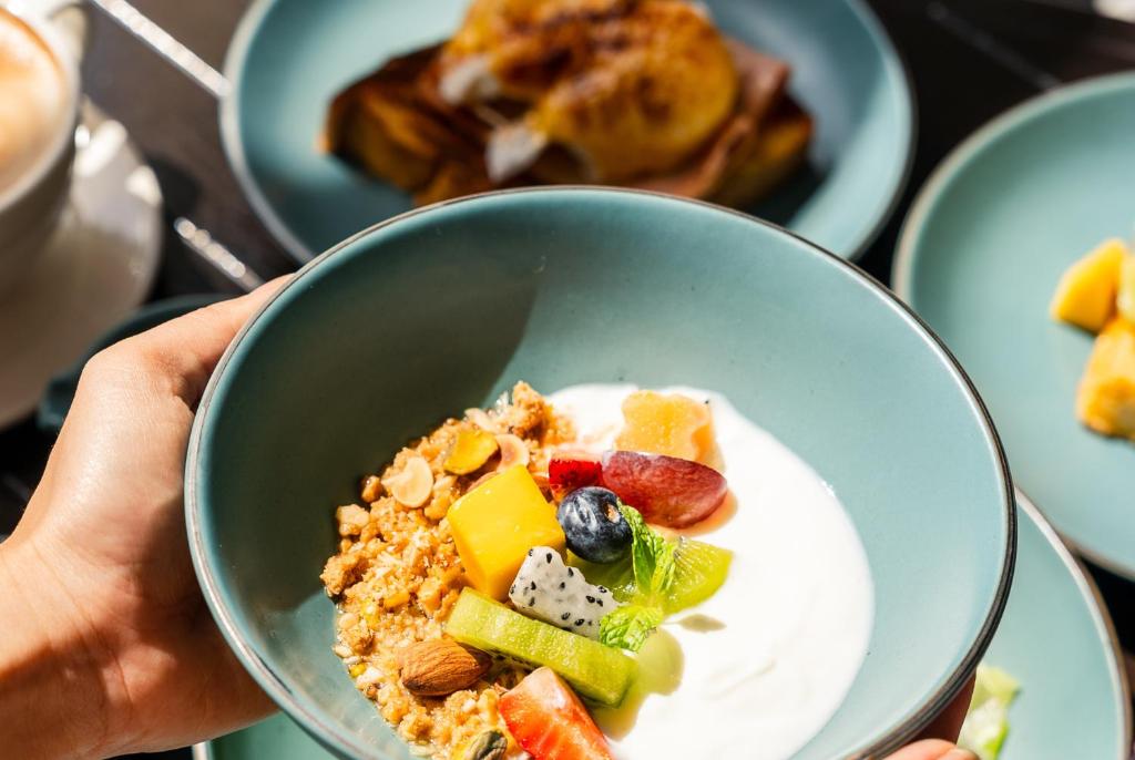 a person holding a bowl of food with fruit and yogurt at Wave Hotel Pattaya in Pattaya