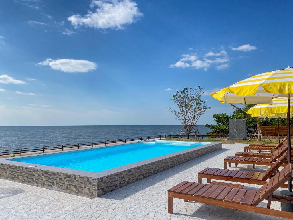 une piscine avec des chaises et un parasol et l'océan dans l'établissement Charome Resort, à Ban Suan On