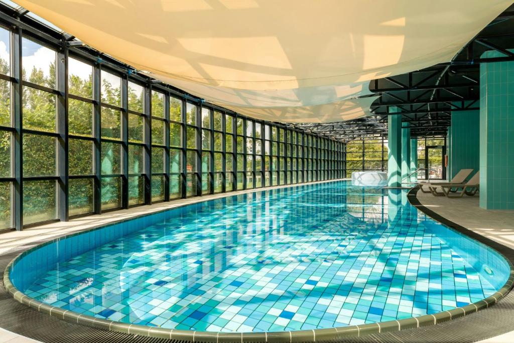 バドフーフェドルプにあるCorendon Amsterdam Schiphol Airport, a Tribute Portfolio Hotelの窓のある建物内に青いタイルの大型スイミングプールがあります。