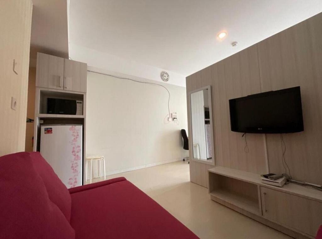 Studio Almahyra Alana Jogja في Kejayan: غرفة معيشة مع أريكة حمراء وتلفزيون بشاشة مسطحة