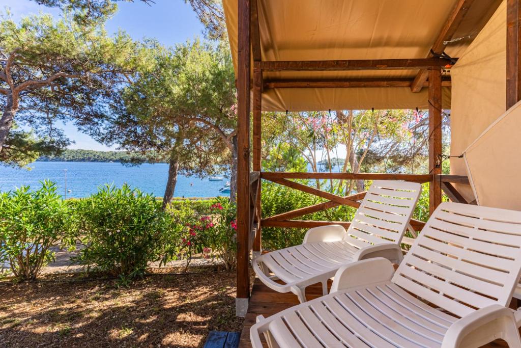 two white chairs on a porch with a view of the water at Adria Glamping luxury tents Camping Poljana Mali Lošinj in Mali Lošinj