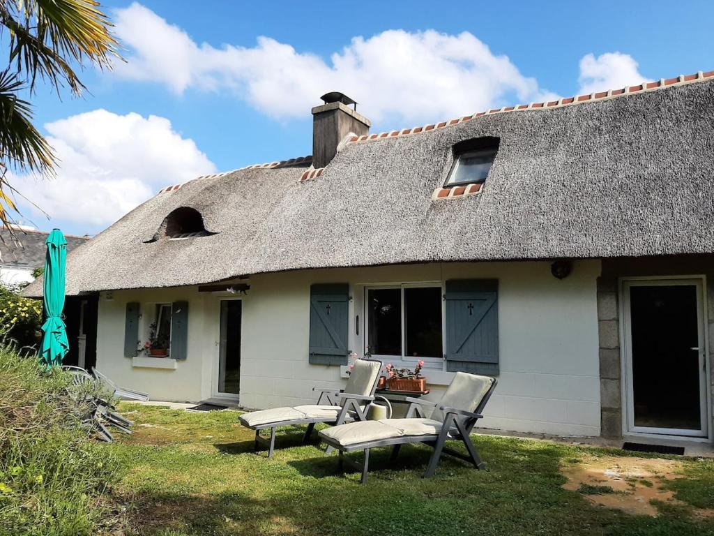 une maison au toit de chaume avec deux chaises et une table dans l'établissement Adorable Chaumière traditionnelle plage à pied, à Fouesnant