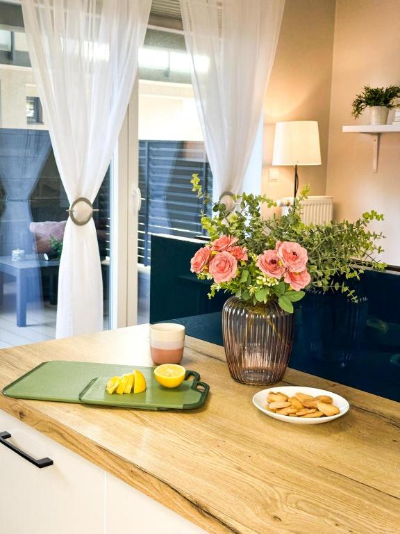 a table with a plate of food and a vase with flowers at Apartamenty Prestige Harmony Rosiczkowa in Augustów