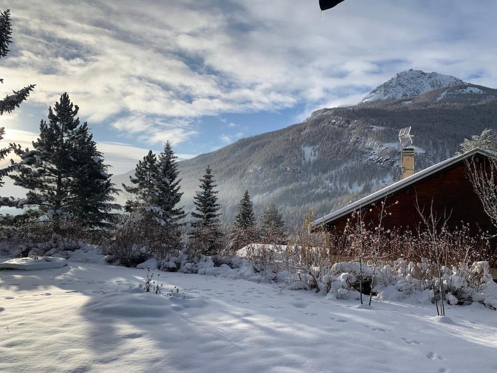 a snow covered cabin with a mountain in the background at Maison Amore Serre Chevalier in Saint-Chaffrey