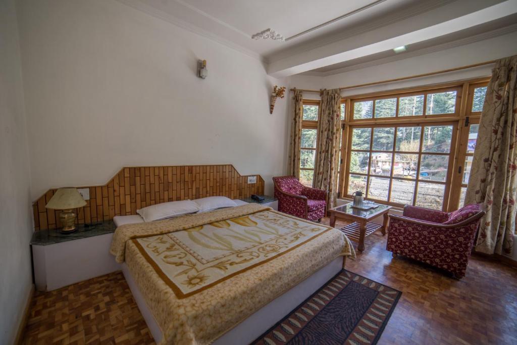a bedroom with a bed and two chairs and windows at Hotel Satkar Residency in Manāli