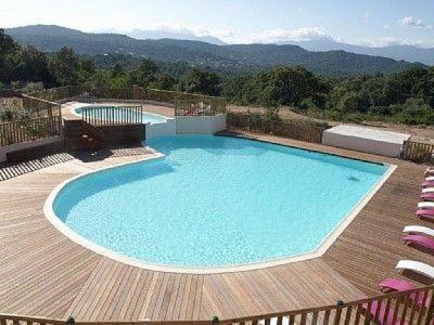 une grande piscine sur une terrasse en bois avec des chaises dans l'établissement Appartement design, à Porto-Vecchio
