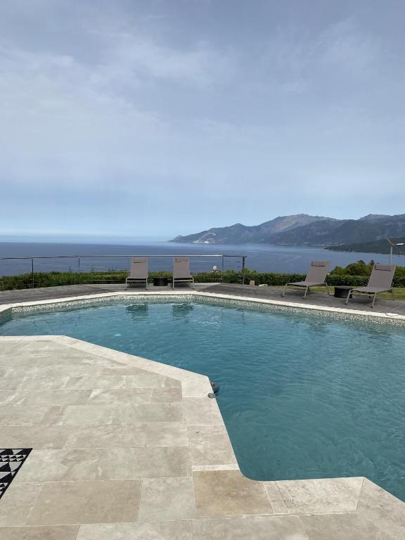 une piscine avec des chaises et l'océan en arrière-plan dans l'établissement Villa d exception vue mer panoramique piscine, à Saint-Florent