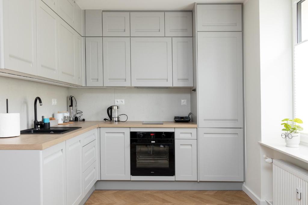 a white kitchen with white cabinets and a black dishwasher at Sekwoja Rent - Malmeda 15 in Białystok