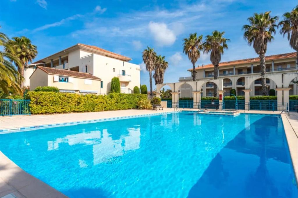 une piscine devant un immeuble avec des palmiers dans l'établissement Domaine d'Azur - Renovated 1BR with Terrace Pool & Garage, au Lavandou