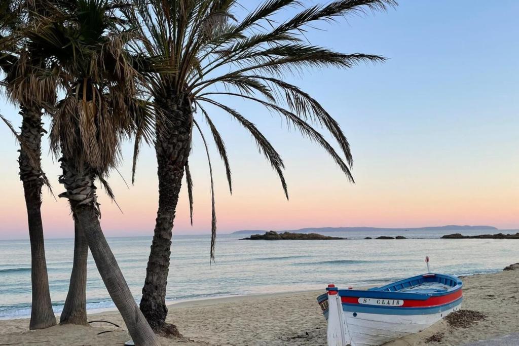 - un bateau sur la plage à côté de deux palmiers dans l'établissement Magnificent T3 - Saint-Clair - 500m from the beach, au Lavandou