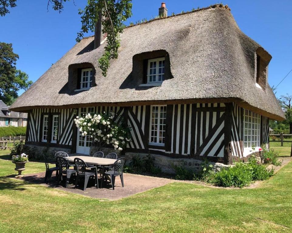 une maison au toit de chaume avec une table et des chaises dans l'établissement Chaumière normande, les pommiers proches de la mer, à Blonville-sur-Mer