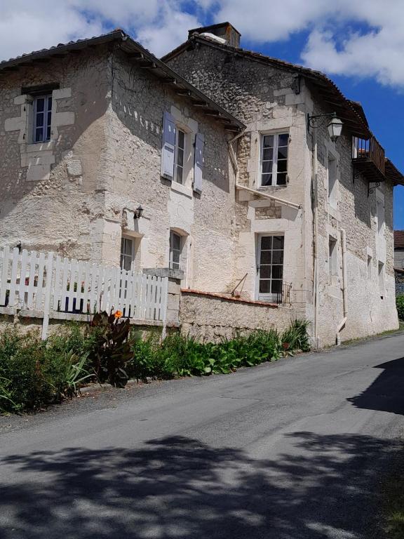 un ancien bâtiment en pierre avec une clôture blanche à côté d'une rue dans l'établissement Lo Vielh Ostal, à Saint-Paul-Lizonne