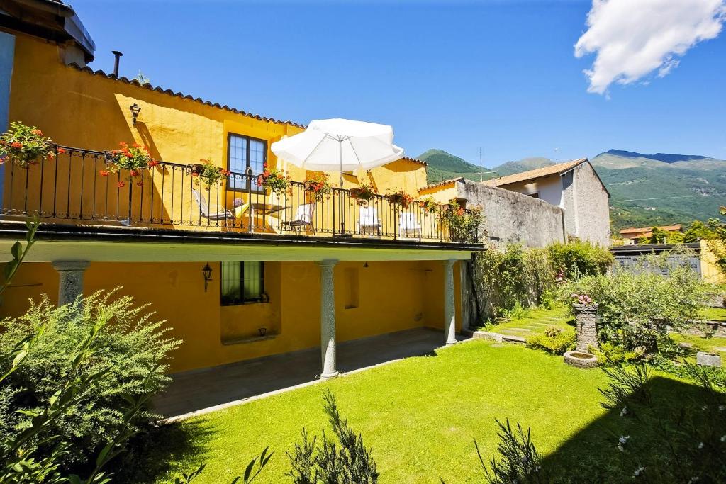 a yellow house with a balcony with an umbrella at Casa Bel Giardino in Cannobio