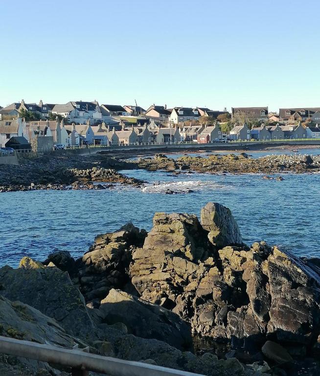 ein Wasserkörper mit Felsen und Häusern im Hintergrund in der Unterkunft Hytheview Cottage Whitehills in Whitehills