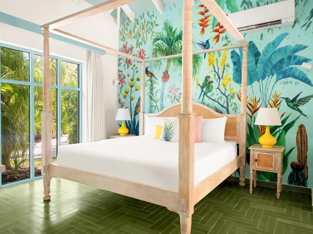 een slaapkamer met een hemelbed en een tropische muurschildering bij Boardwalk Boutique Hotel Aruba - Adults Only in Palm-Eagle Beach