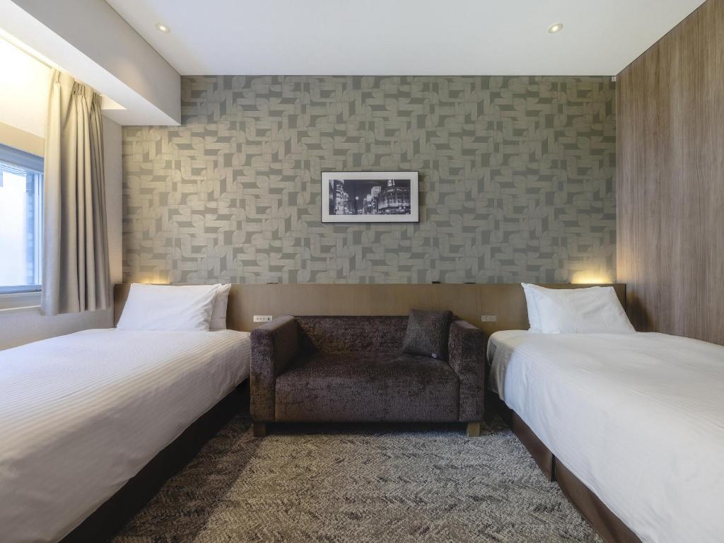 a hotel room with two beds and a chair at Hotel Gracery Ginza in Tokyo
