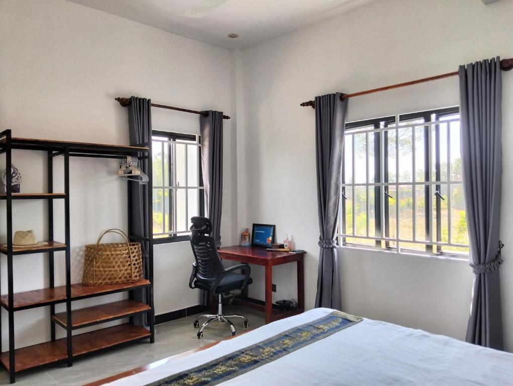 a bedroom with a bed and a desk and windows at Baksaei Retreat Ricefield Villas in Kampot