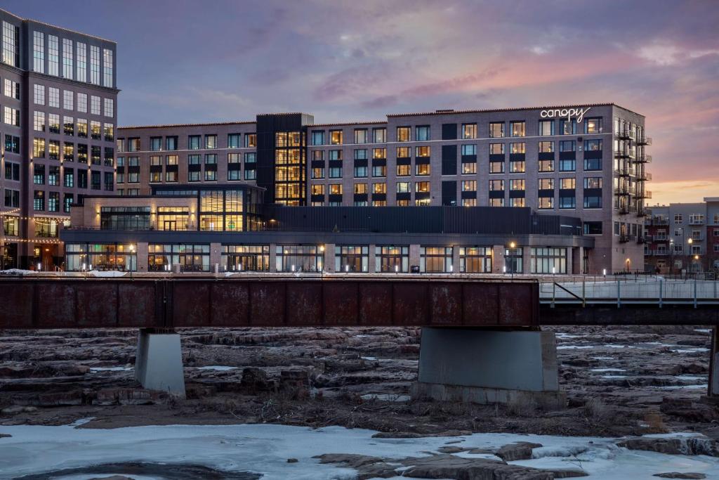 苏福尔斯Canopy By Hilton Sioux Falls Downtown的一座河上的桥梁,有建筑背景