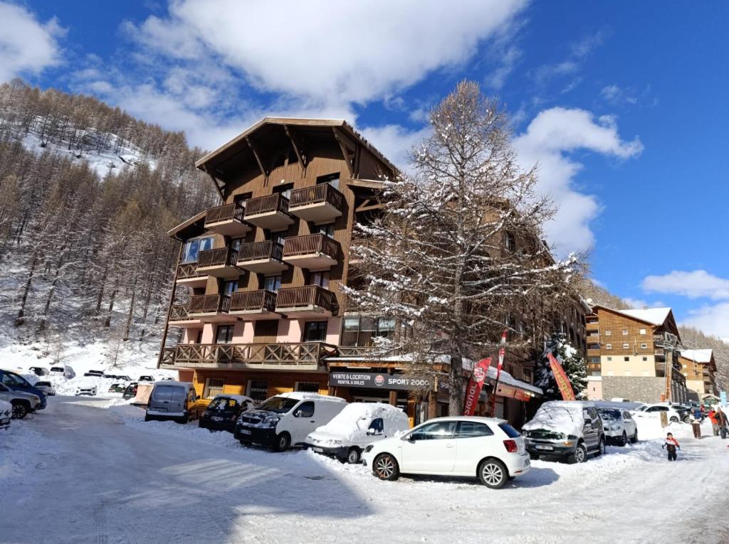 un grand bâtiment avec des voitures garées dans la neige dans l'établissement Studio Val d'allos Mercantour, à Allos