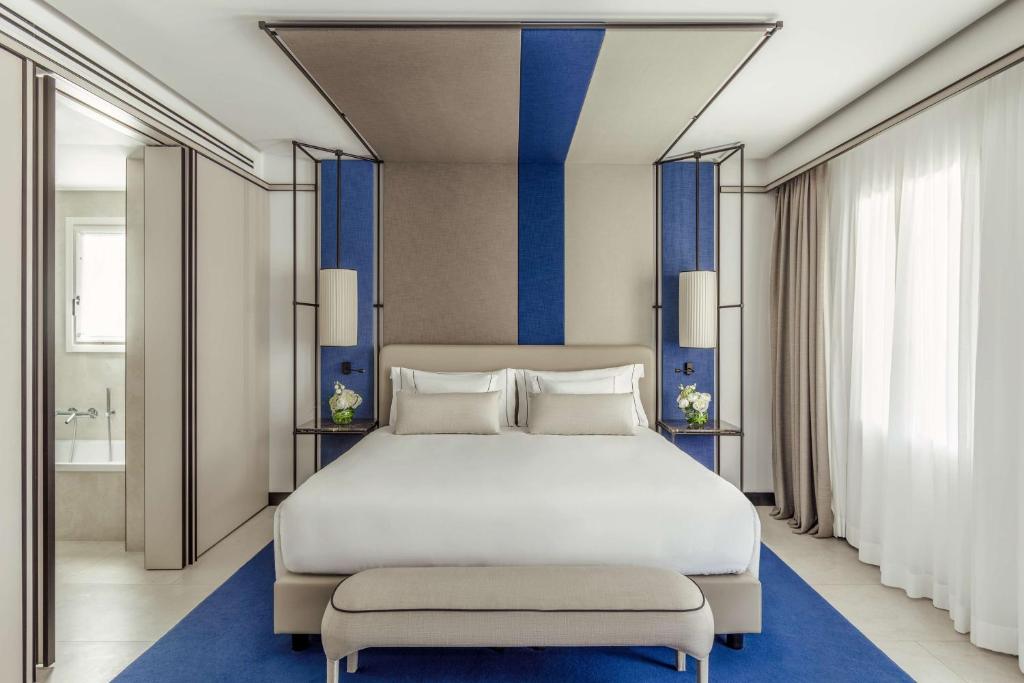 a bedroom with a large white bed with blue stripes at Tivoli Portopiccolo Sistiana Wellness Resort & Spa in Sistiana