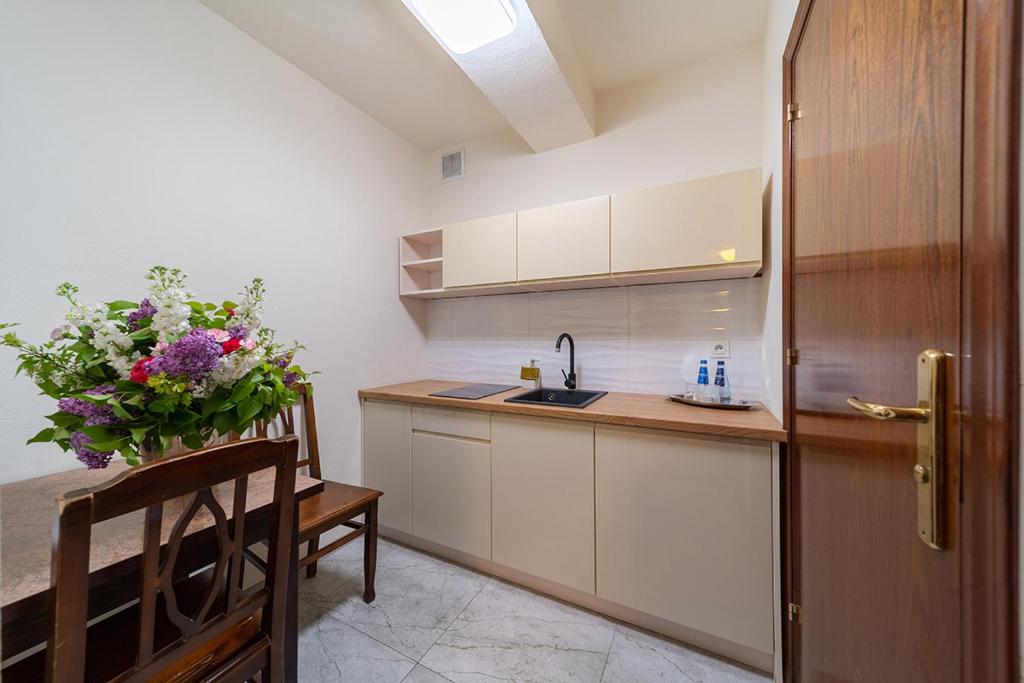Compact kitchen with light cabinetry, floral arrangement, and wooden dining table.