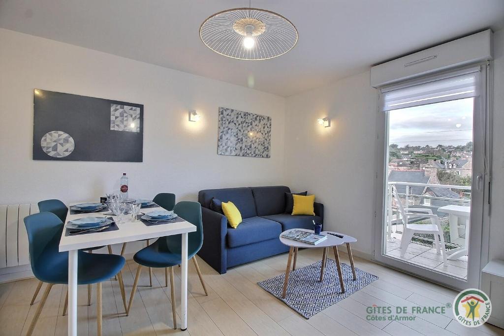 Una sala de estar con un sofá azul y una mesa. en Vue sur la station, en Erquy