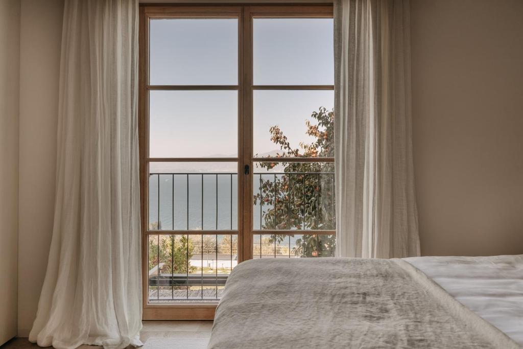 a bedroom with a large window with white curtains and a bed at Borgo SAN SONNEA Lake Garda in Torri del Benaco