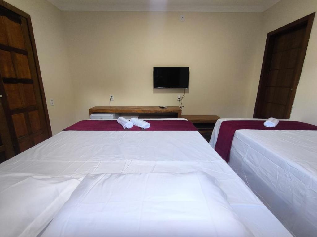 1 dormitorio con 2 camas con sábanas blancas y TV en Vila Bahia suítes, en Caraíva