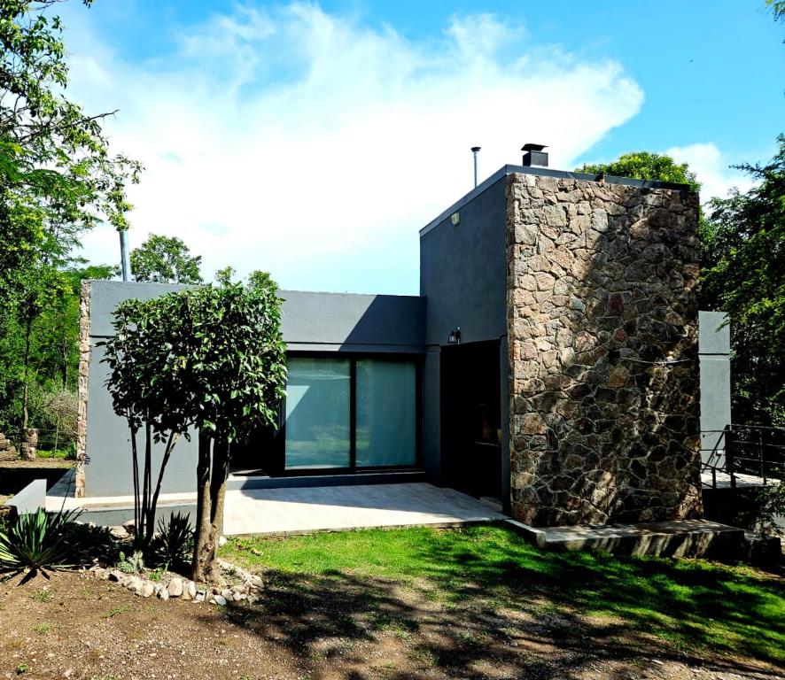 a house with a stone wall and a tree at Cabaña Panpachay Villa Giardino in Villa Giardino