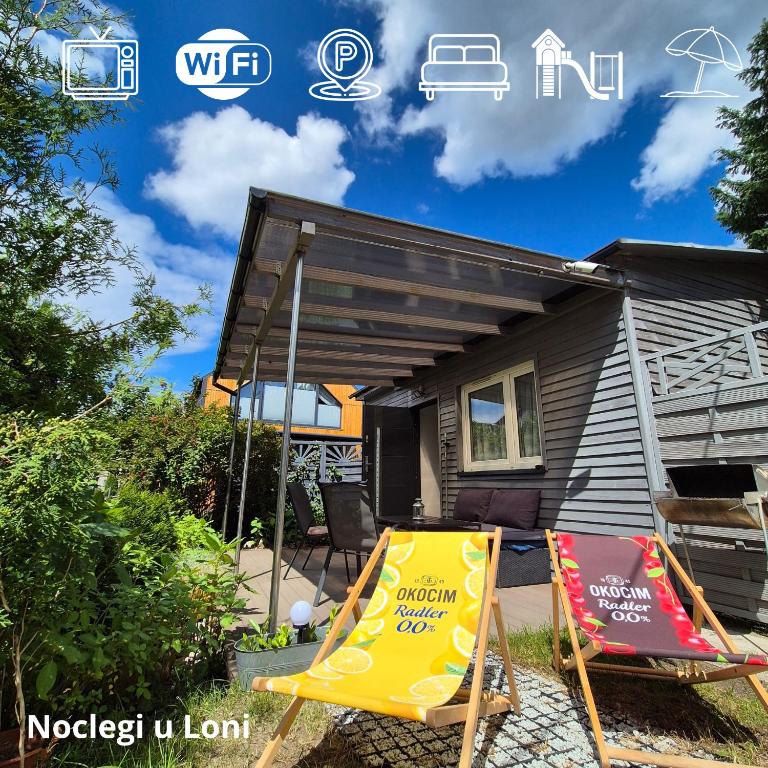 a house with two lawn chairs and a yellow sign at Noclegi u Loni - Szary domek - noclegi w zacisznym centrum Pobierowa nad morzem z parkingiem in Pobierowo