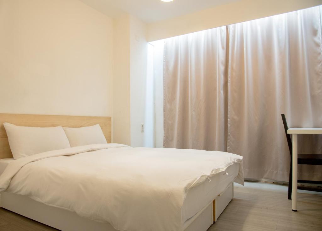 a white bedroom with a bed and a window at Haogong Hotel in Taichung