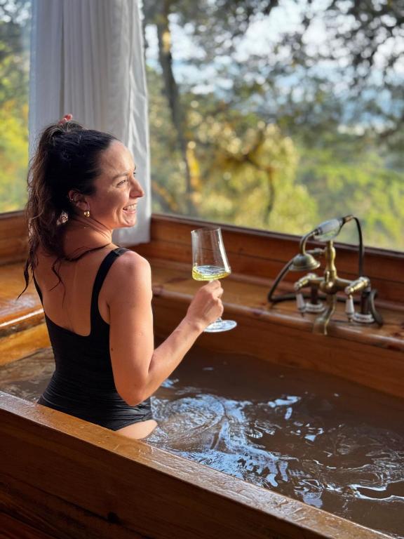 a woman holding a glass of wine in a bathtub at Chalés Recanto do Vale - TUCANO in Bom Jardim da Serra
