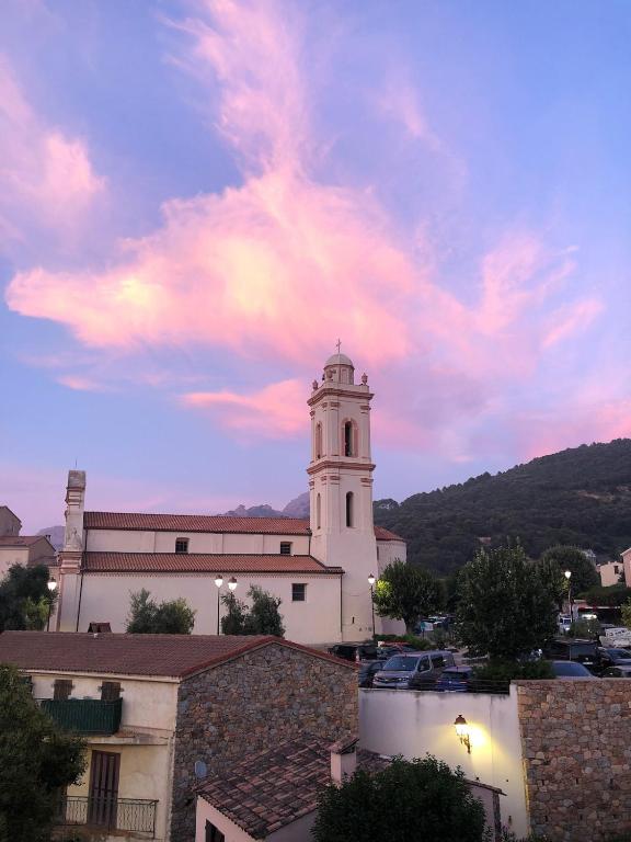 un bâtiment blanc avec une tour d'horloge et un ciel nuageux dans l'établissement Duplex au coeur du village, à Piana