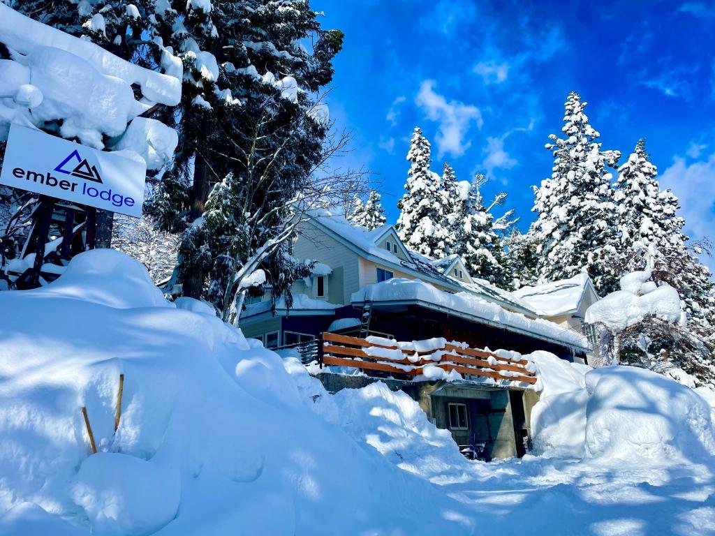 a house covered in snow with trees and a sign at Ember Lodge - Hakuba in Hakuba