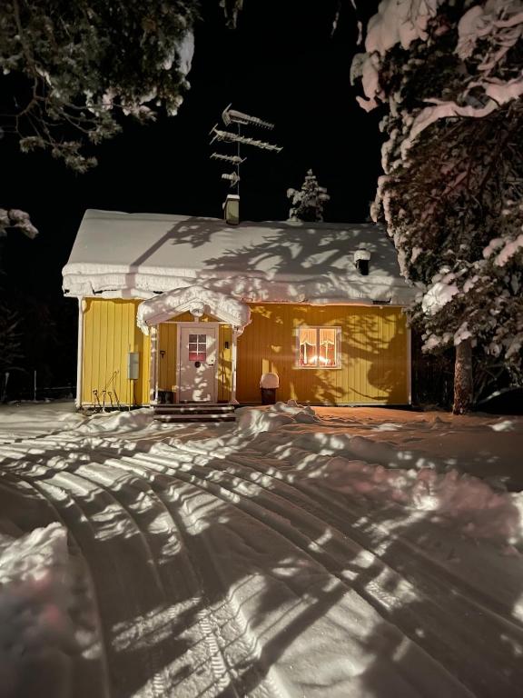 a yellow house with snow on the roof at night at Mysigt hus på hästgård, mellan Jukkasjärvi och Kiruna in Kiruna