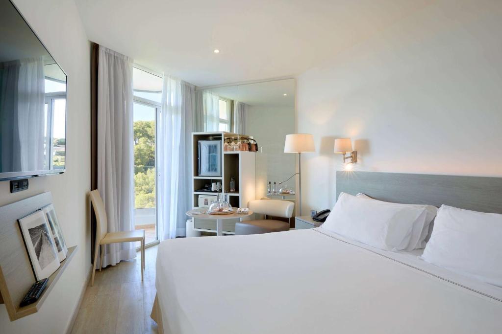 a bedroom with a large white bed and a desk at Meliá Cala Galdana in Cala Galdana