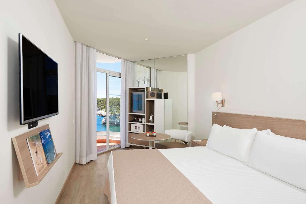 a bedroom with a bed and a television and a table at Meliá Cala Galdana in Cala Galdana