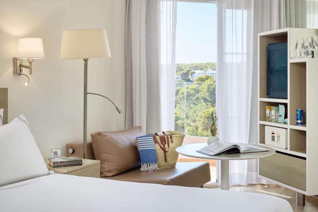 a bedroom with a bed and a table and a window at Meliá Cala Galdana in Cala Galdana
