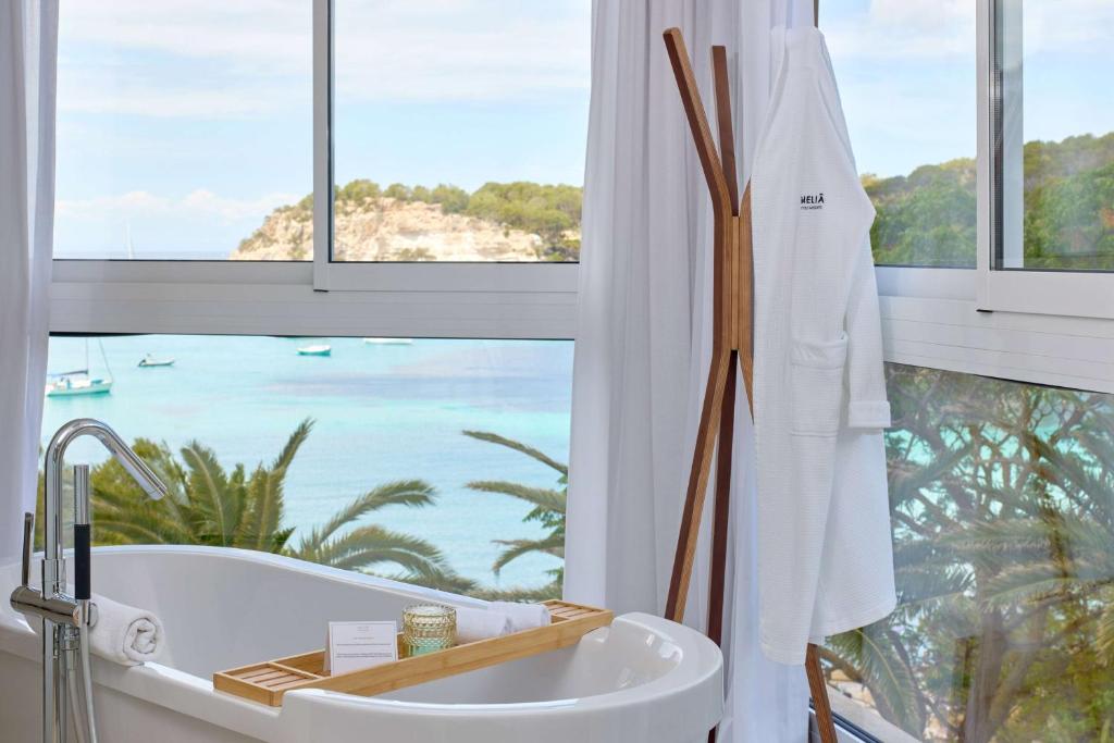 a bath tub in a bathroom with a view of the ocean at Meliá Cala Galdana in Cala Galdana